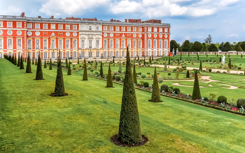 Tourists exploring Privy Gardens at Hampton Court Palace on a sunny day.