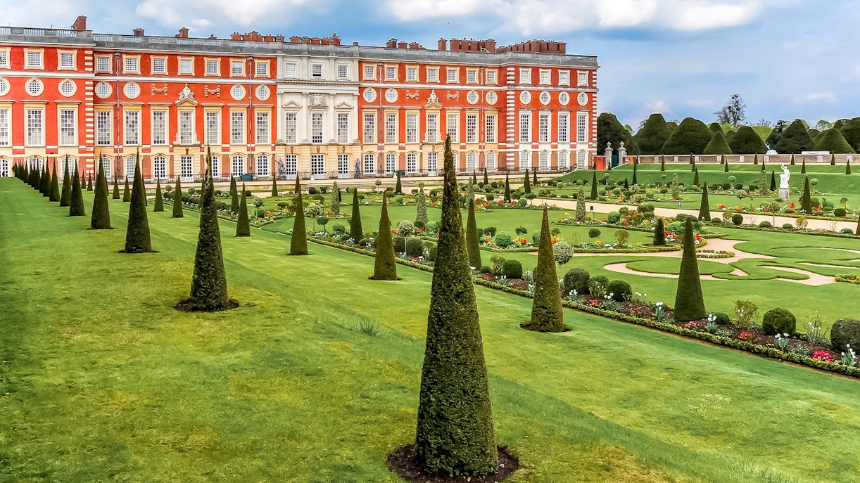 Tourists exploring Privy Gardens at Hampton Court Palace on a sunny day.