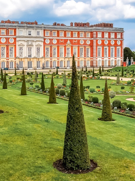 Tourists exploring Privy Gardens at Hampton Court Palace on a sunny day.