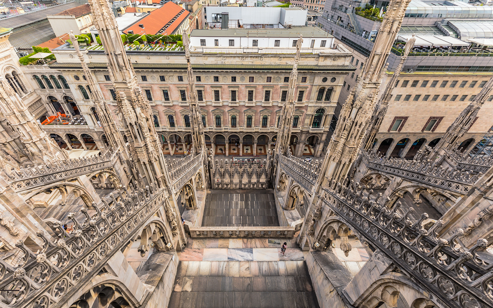 Rooftop view of Milan Duomo Cathedral's intricate spires overlooking city buildings.