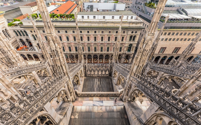 Rooftop view of Milan Duomo Cathedral's intricate spires overlooking city buildings.