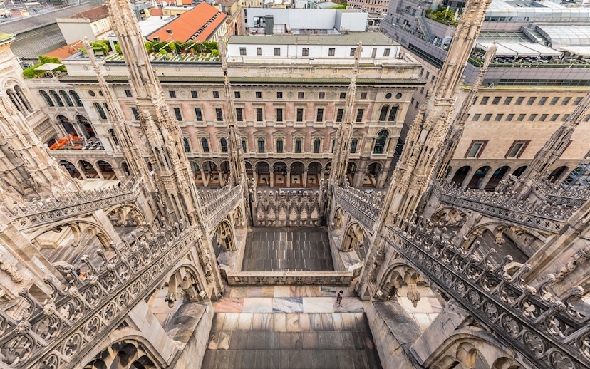 Rooftop view of Milan Duomo Cathedral's intricate spires overlooking city buildings.