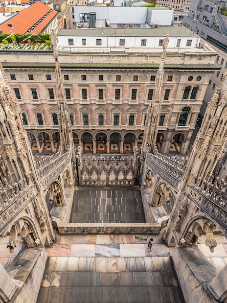 Rooftop view of Milan Duomo Cathedral's intricate spires overlooking city buildings.