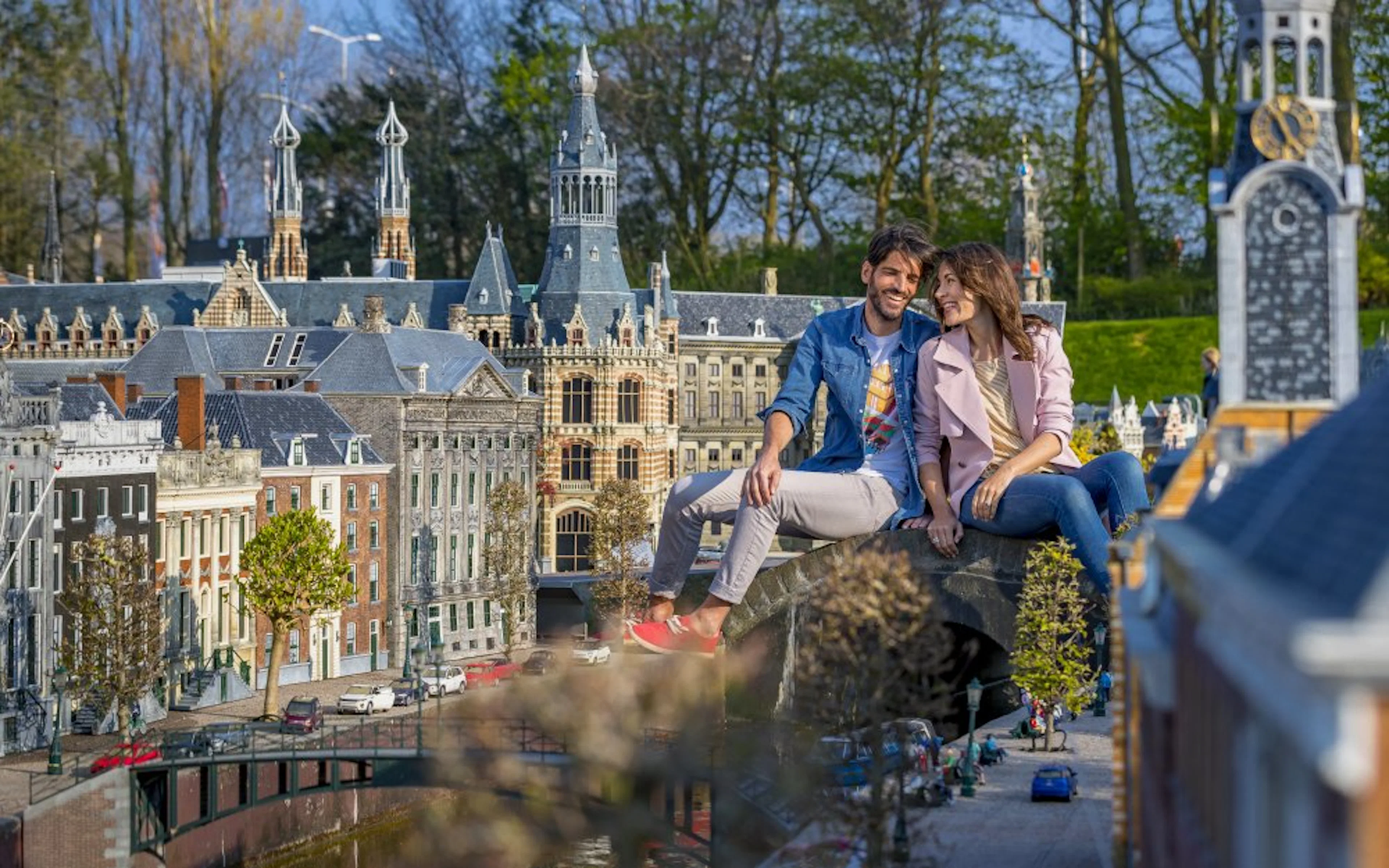 Couple sitting on a bridge at Madurodam miniature park, Netherlands, with detailed model buildings.