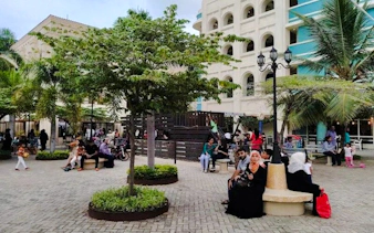 People relaxing in a plaza with trees and a building in Masaki, Dar es Salaam.