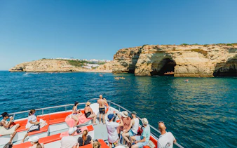 Tourists on a boat enjoying views of Albufeira's coastal cliffs during a cruise and beach BBQ.