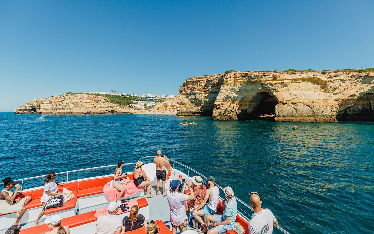 Tourists on a boat enjoying views of Albufeira's coastal cliffs during a cruise and beach BBQ.