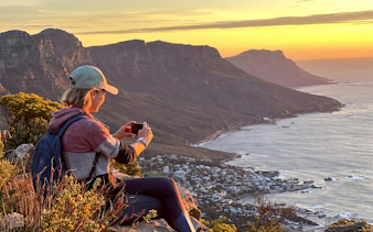 Person taking photo of Cape Town coastline from Lion's Head at sunrise.