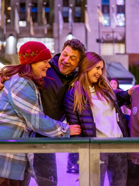 Tourists ice skating at The Rink with festive lights in the background.