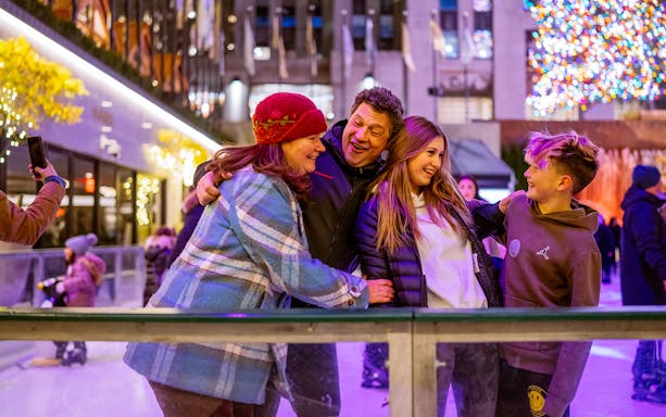 Tourists ice skating at The Rink with festive lights in the background.
