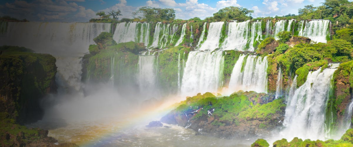 Waterfalls cascading over lush cliffs with a rainbow at Iguazu Falls, Argentina.