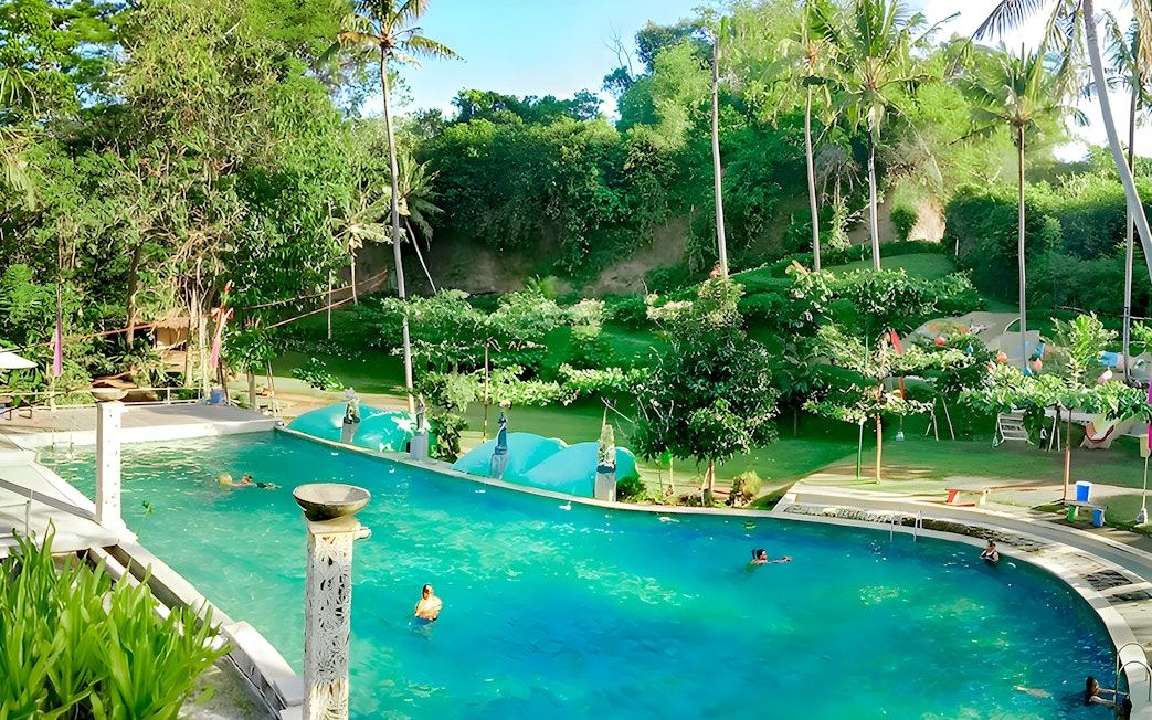 Keramas Park pool with swimmers surrounded by lush greenery and palm trees.