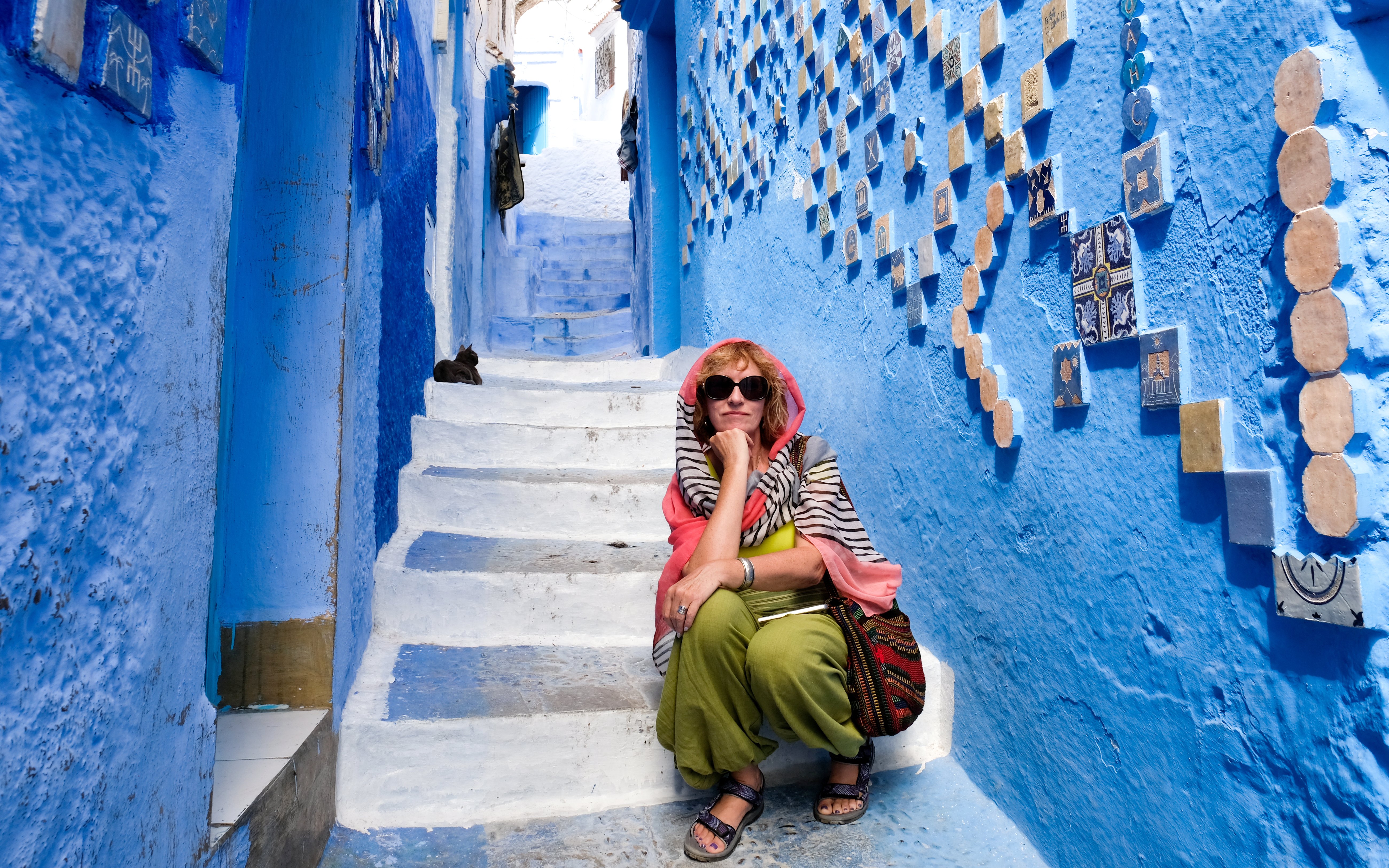 Tourist sitting on blue-painted stairs in Chefchaouen, Morocco.
