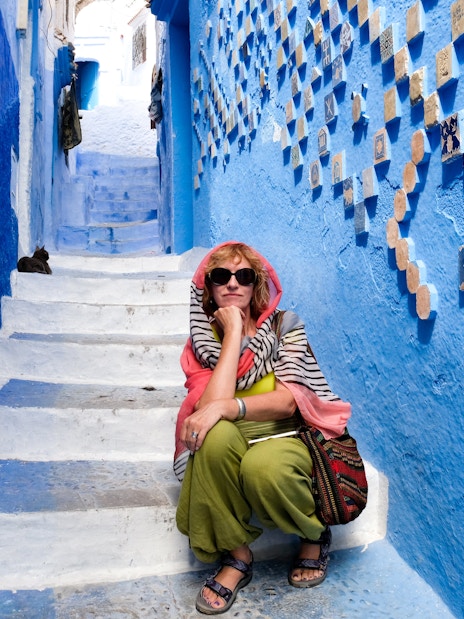Tourist sitting on blue-painted stairs in Chefchaouen, Morocco.