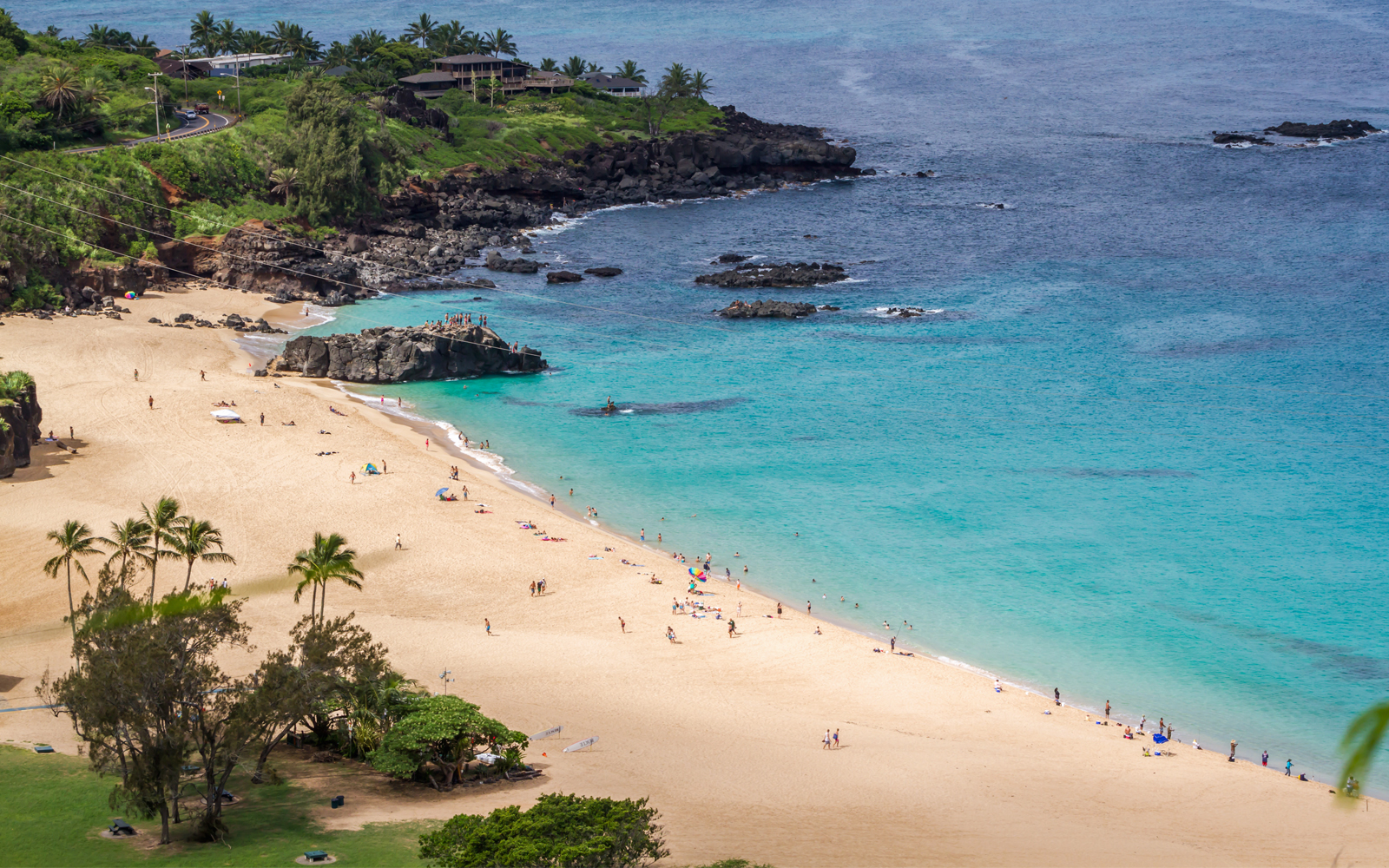 Waimea Bay Beach Park with visitors on sandy shore and turquoise water, Oahu, Hawaii.