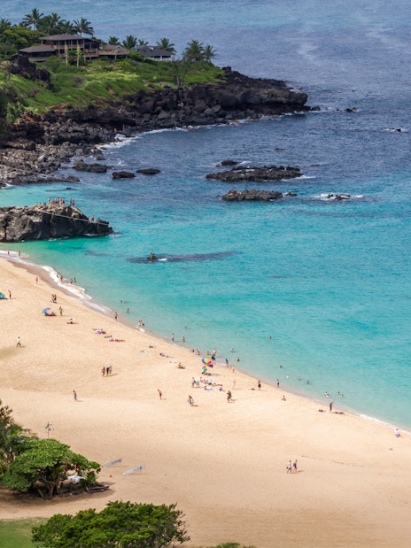 Waimea Bay Beach Park with visitors on sandy shore and turquoise water, Oahu, Hawaii.
