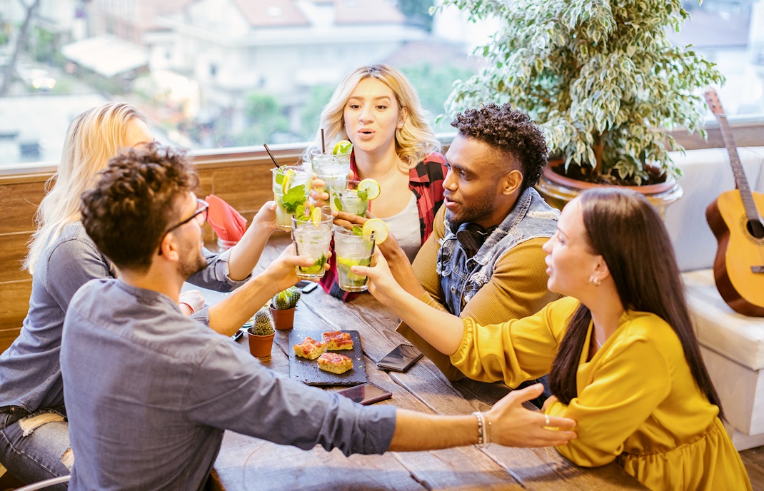 Group of young people toasting with mojito cocktails at a dining table.