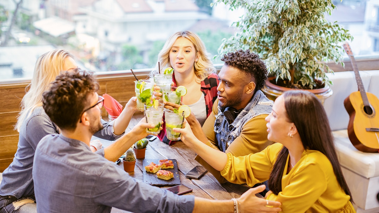 Gruppe junger Leute, die an einem Esstisch mit Mojito-Cocktails anstoßen.