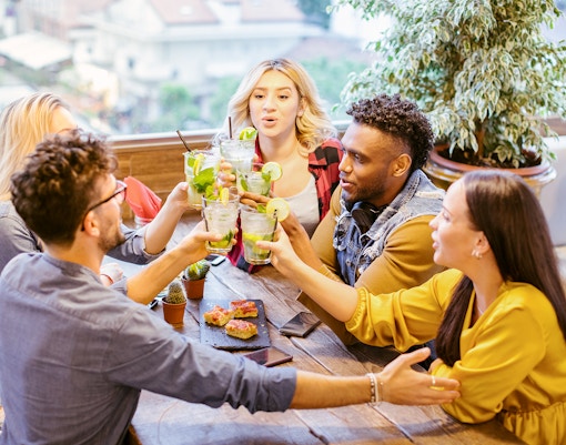 Group of young people toasting with mojito cocktails at a dining table.
