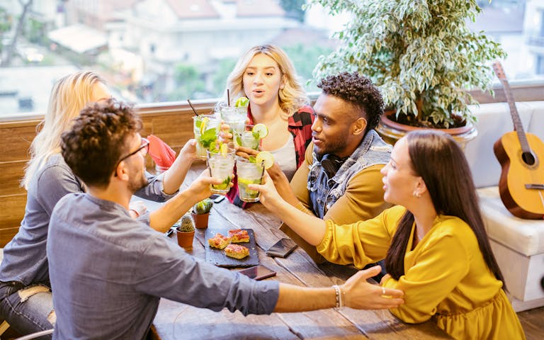 Group of young people toasting with mojito cocktails at a dining table.