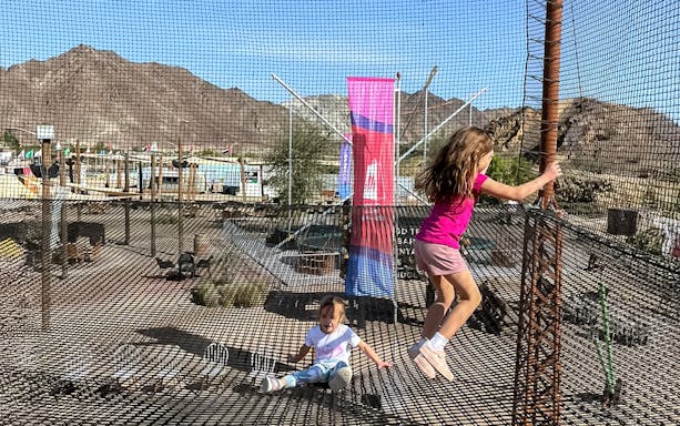 Children playing on a netted trampoline at Hatta Wadi Hub with mountains in the background.