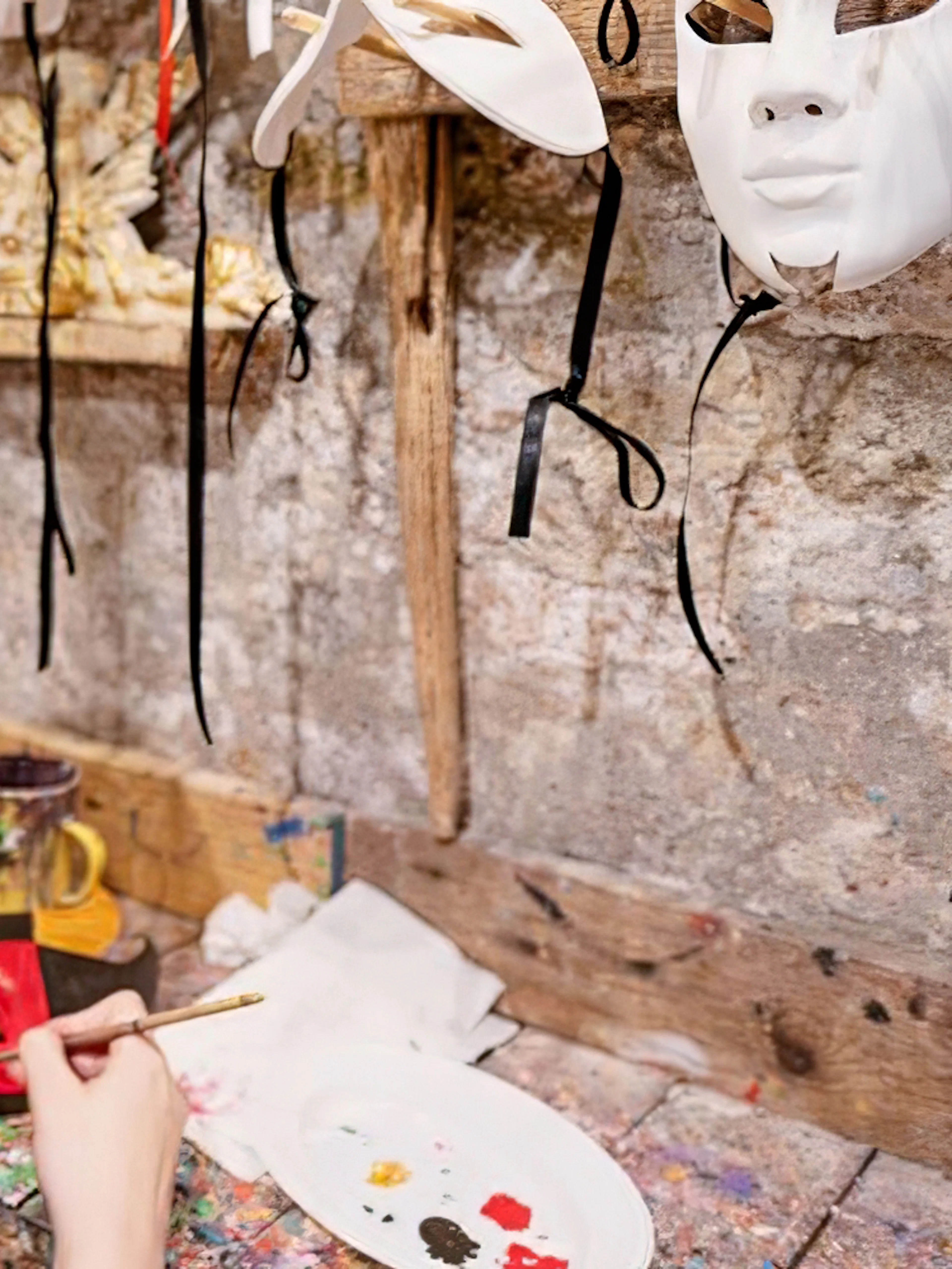 Person painting a colorful mask at a workshop with masks hanging on the wall.