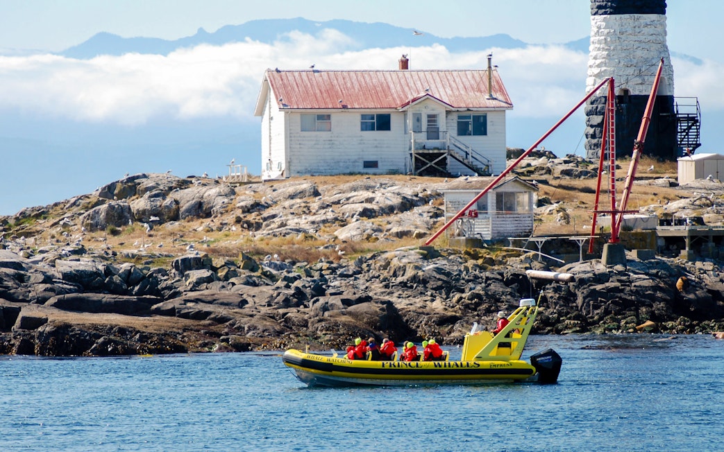 Prince of Whales boat with passengers in red life jackets near a rocky island with a lighthouse.