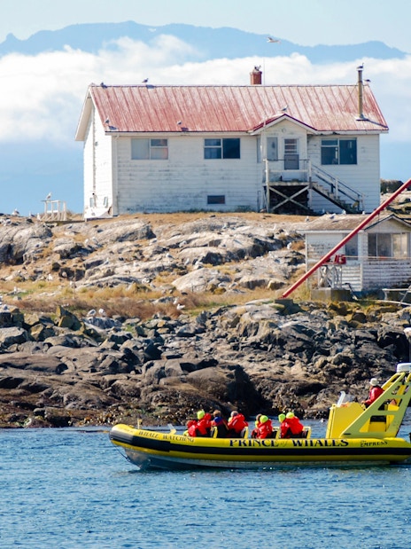 Prince of Whales boat with passengers in red life jackets near a rocky island with a lighthouse.