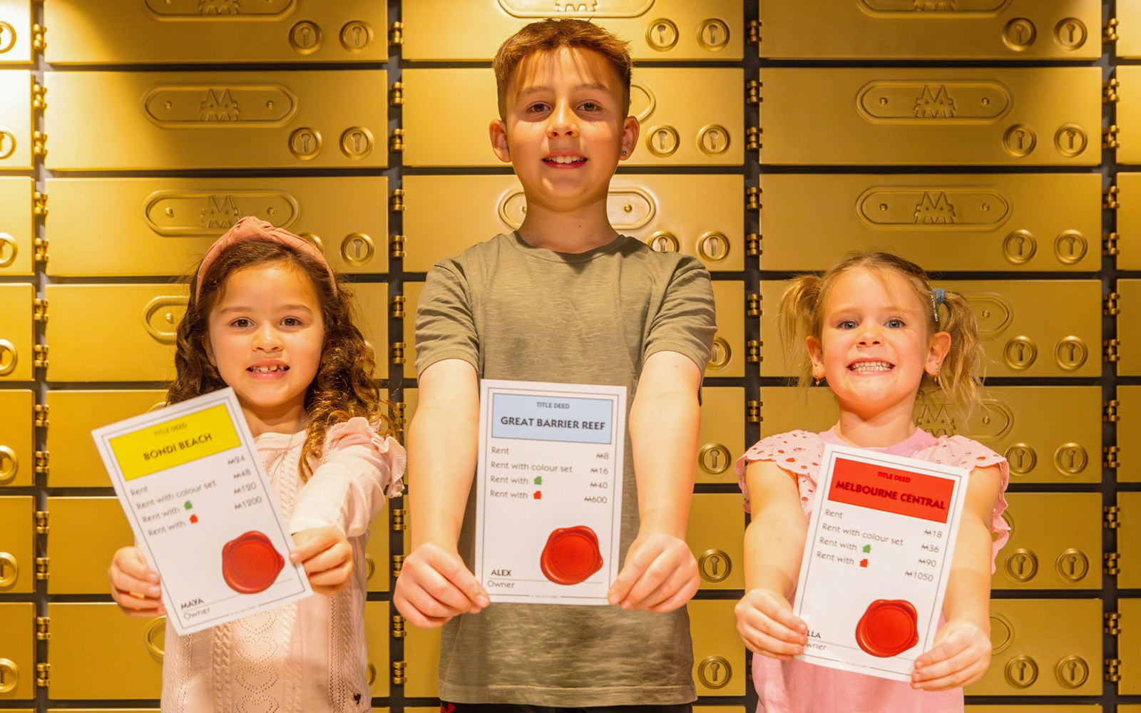 Children holding Monopoly property cards at Monopoly Dreams Melbourne exhibit.