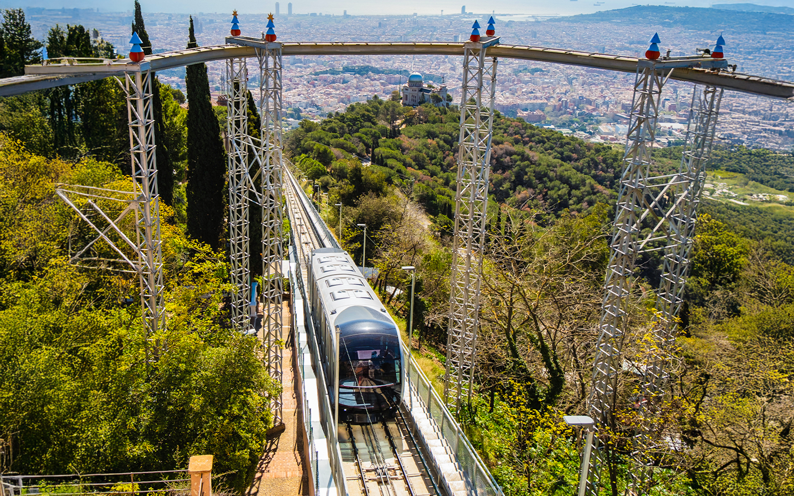 Tibidabo funicular ascending through lush greenery with Barcelona cityscape in the background.