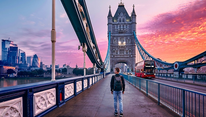 Person walking on Tower Bridge in London at sunset with city skyline in background.