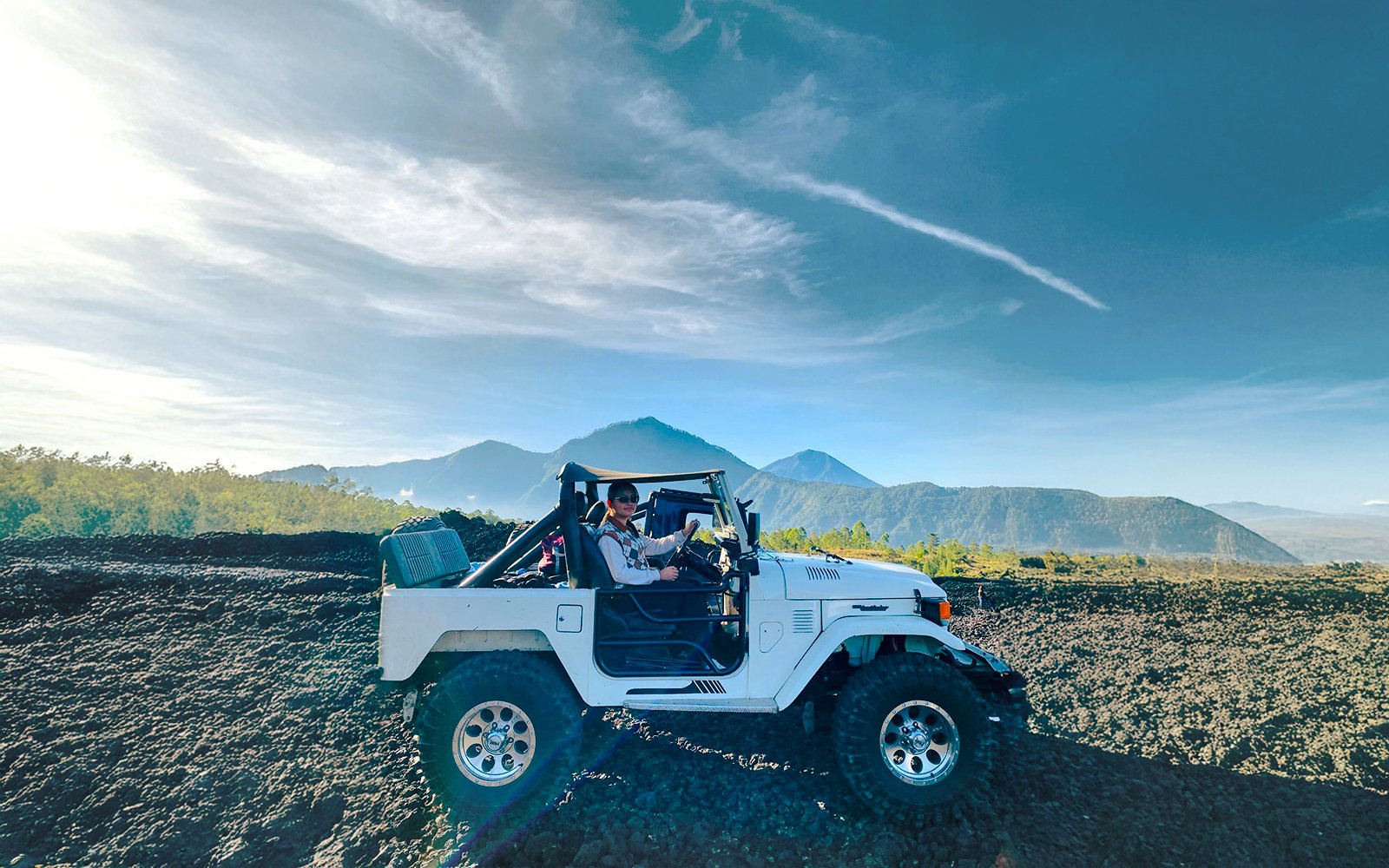 Off-road vehicle on black lava field with Mount Batur in Bali.