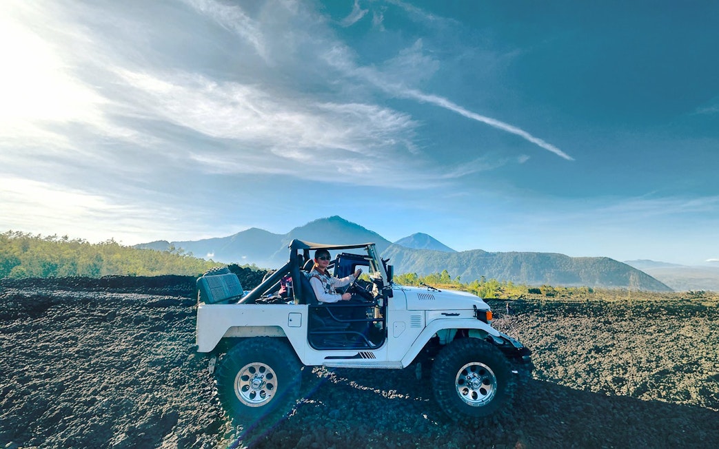 Off-road vehicle on black lava field with Mount Batur in Bali.