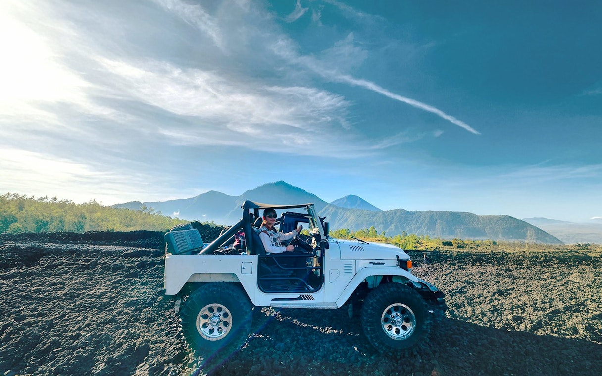 Off-road vehicle on black lava field with Mount Batur in Bali.