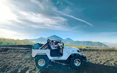 Off-road vehicle on black lava field with Mount Batur in Bali.