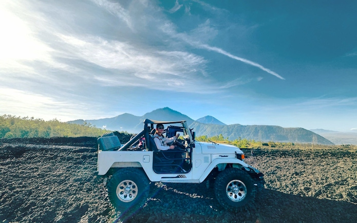 Off-road vehicle on black lava field with Mount Batur in Bali.