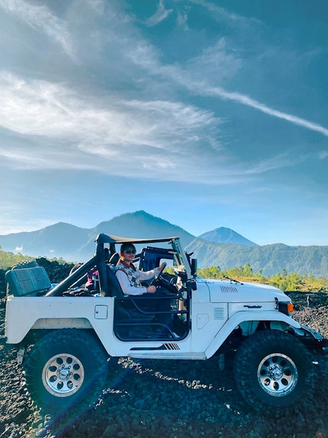 Off-road vehicle on black lava field with Mount Batur in Bali.