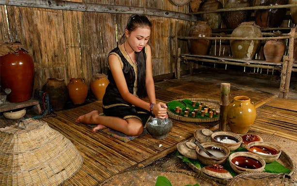 Woman preparing traditional food at Mari Mari Village, surrounded by pottery and bamboo utensils.