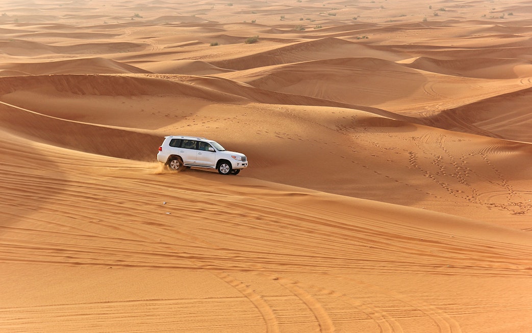SUV driving on desert dunes during an evening safari with quad bike option.