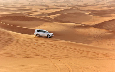 SUV driving on desert dunes during an evening safari with quad bike option.