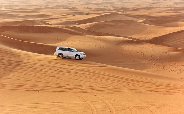 SUV driving on desert dunes during an evening safari with quad bike option.