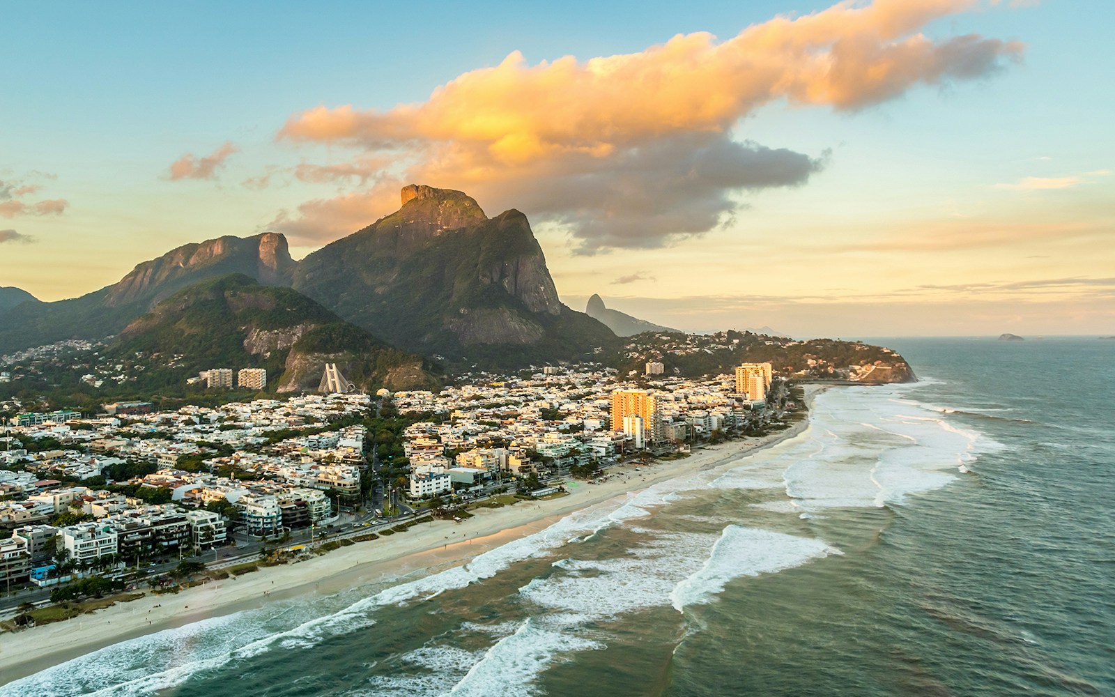Aerial view of Rio de Janeiro from a helicopter at sunset, highlighting Sugarloaf Mountain and Guanabara Bay.