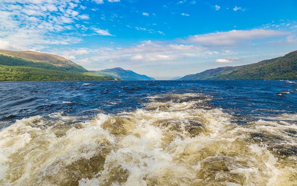 Wake from a high-speed boat on Loch Ness with surrounding hills.