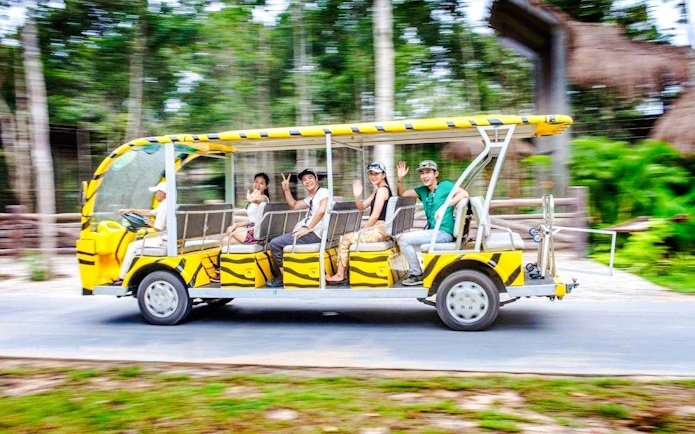 Tourists riding a yellow zoo tram car through a lush, green environment.