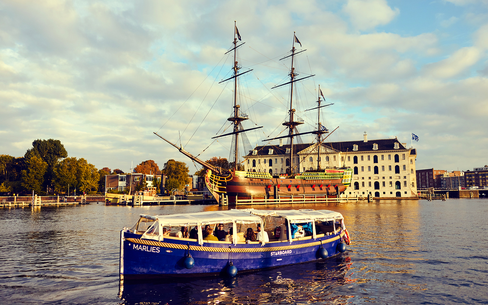 Amsterdam canal cruise boat near historic ship and maritime museum.