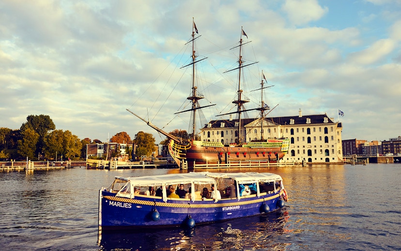 Amsterdam canal cruise boat near historic ship and maritime museum.