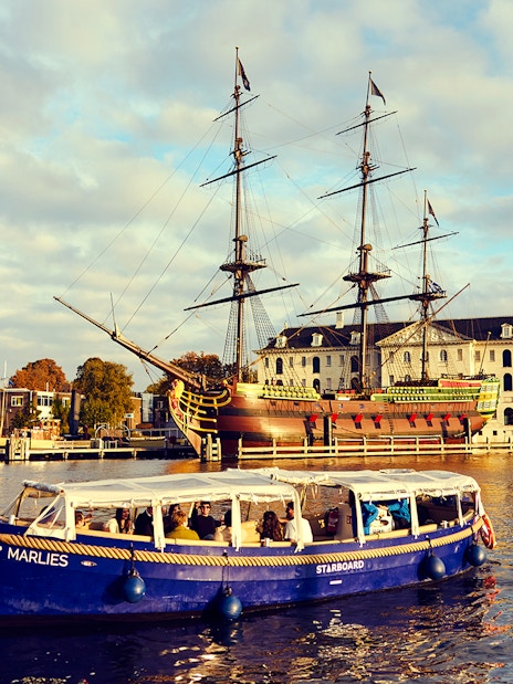 Amsterdam canal cruise boat near historic ship and maritime museum.