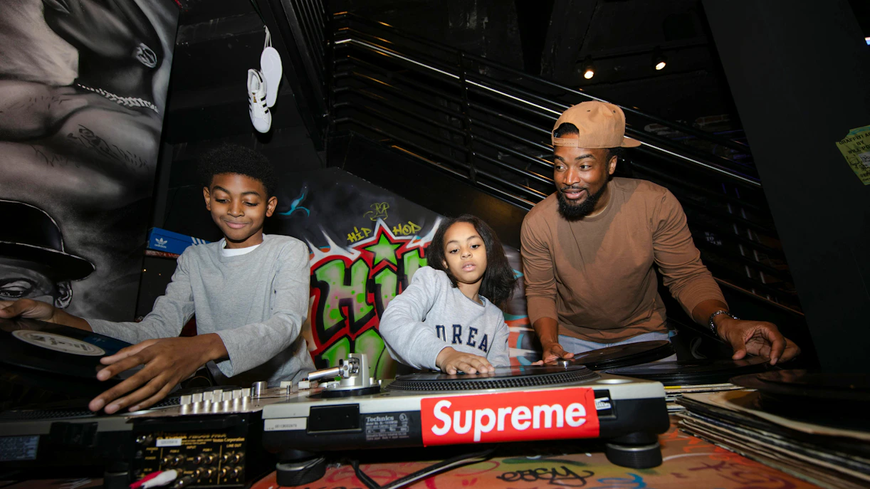 Guests playing DJ console at RiseNY with graffiti backdrop.