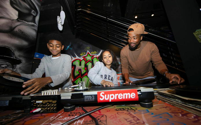 Guests playing DJ console at RiseNY with graffiti backdrop.