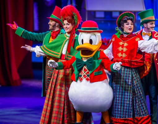 Performers in festive costumes with a duck character on stage at a holiday show.